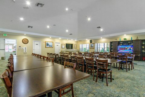 A room with tables and chairs and a TV on the wall.